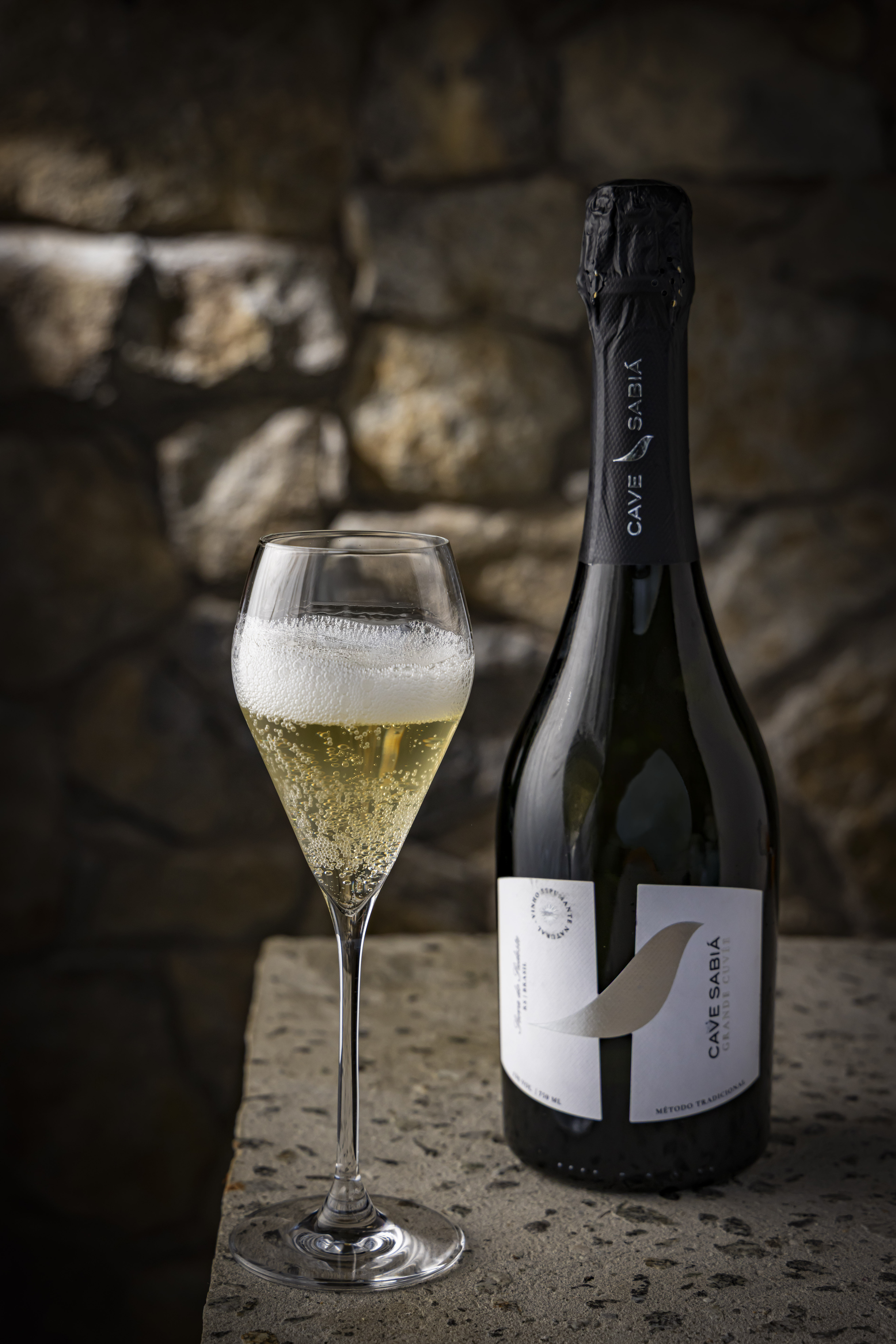 Garrafa e taça de Cave Sabiá entre pedras